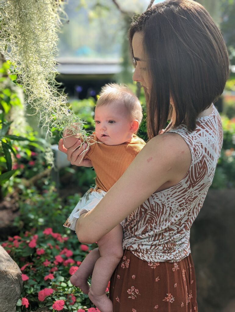 Mother holding daughter as she reaches out to touch a plant